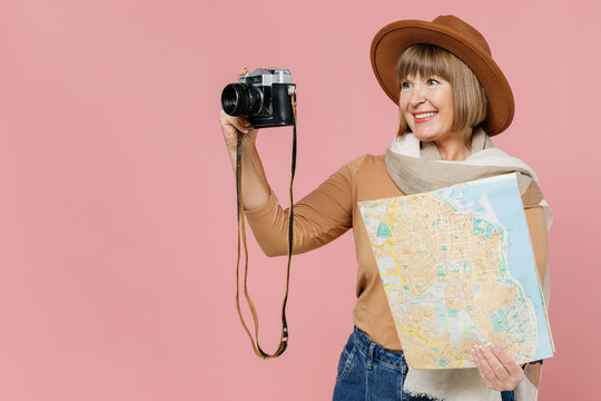 Traveler tourist mature elderly senior lady woman 55 years old wear brown shirt hat scarf hold retro vintage photo camera map look aside isolated on plain pastel light pink background studio portrait
