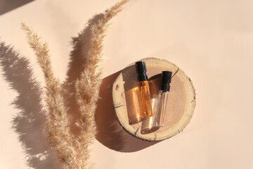 Two glass perfume samples on a wooden tray lying on a beige background with pampas grass. Luxury...