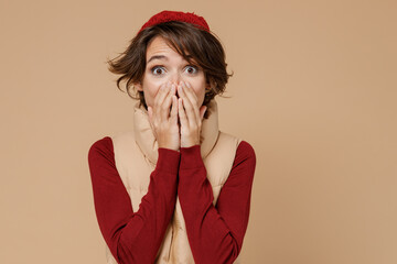 Young surprised woman 20s wearing red turtleneck yellow vest beret looking camera covering mouth...