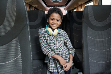Happy cute little schoolboy in casualwear standing in aisle between two rows of seats inside bus