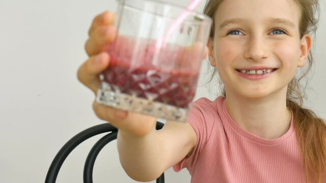 Sweet little girl drinks raspberry smoothie and smiles. Vegetarian drink. Close-up portrait of a child who enjoys a refreshing tasty raspberry juice, healthy eating