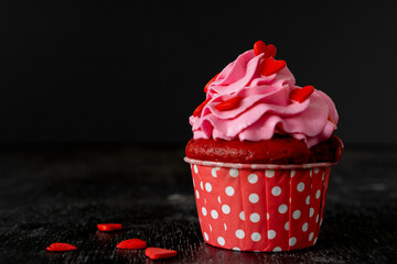 Valentine's day cupcake is decorated with raspberries, red hearts on black background. Copy space. Delicious delicacy. Muffin with cream. Cake. low key