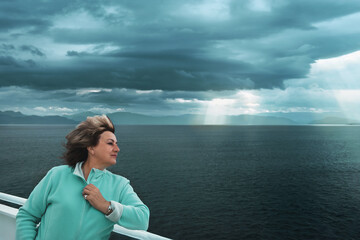 Fototapeta premium beautiful mature woman puts her face to the wind. Ferry ride on the North Sea, Norway. Portrait of a mature active woman. copy space