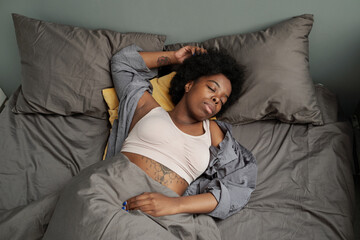 Fototapeta na wymiar Young tired African woman sleeping in double bed with two pillows at night