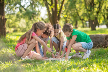 Children with map and magnifying glass on lawn