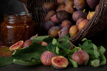 a basket of fresh figs and a jar of fig jam on a dark gray background