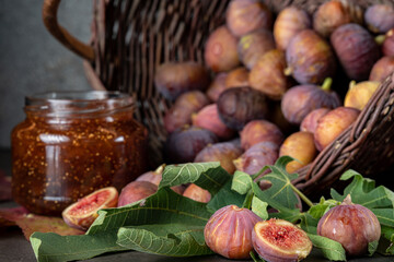 Obraz na płótnie Canvas a basket of fresh figs and a jar of fig jam on a dark gray background