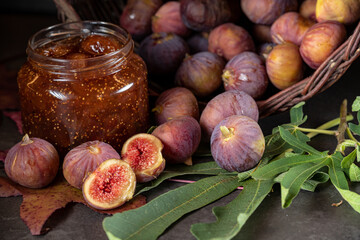 a basket of fresh figs and a jar of fig jam on a dark gray background