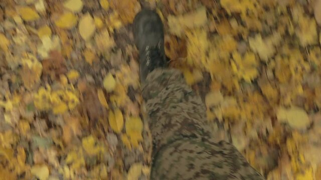 a man in camouflage and black boots walks in the forest on yellow fallen leaves
