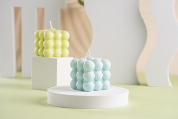 One blue square bubble candle on a white oval and an off-white candle on a cube in the back