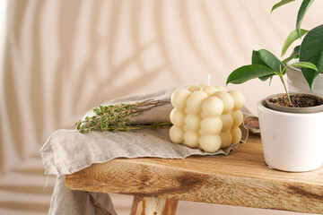 An off-white square bubble candle on a linen cloth on a rustic wooden table with plants at a tropical setting