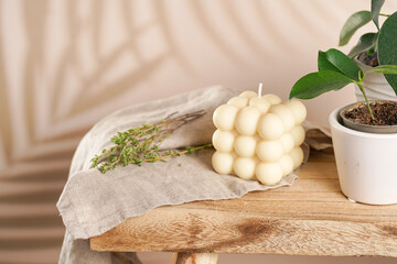 An off-white square bubble candle on a linen cloth on a rustic wooden table with plants at a...
