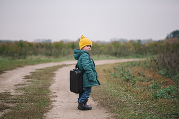 Little caucasian boy carring big case with drone in the field, side view