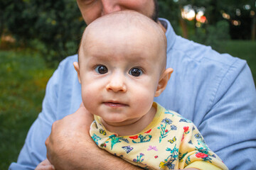 Dad holds his baby son in his arms close-up outdoors. Kid looking at the camera. Father and his newborn son on the background of a summer landscape