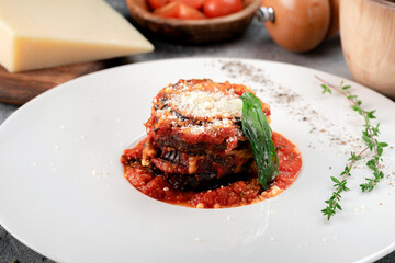 Baked eggplant in tomato sauce with basil and cheese on a white plate. Parmigiana di melanzane dish