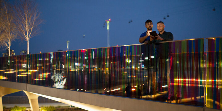 Men with smart phone on illuminated footbridge in city at night, London