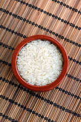 Bowl filled with white raw basmati rice grains with bamboo background