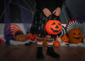 Close-up child legs in witch costume with Jack o' lantern candy bucket. Concept of Halloween