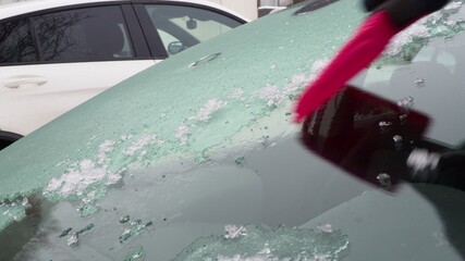 A woman is cleaning an icy window on a car with ice scraper. Focus on the ice scraper. Cold snowy and frosty morning.