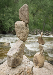 Granite stacked rocks balance on a boulder overlooking a flowing stream river in sunny mountain forest