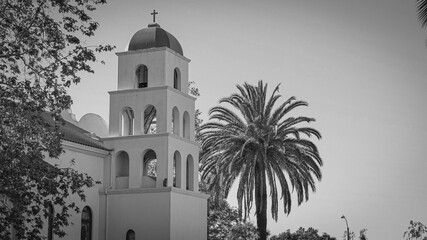 Small stucco Catholic church with bell tower surrounded by palm trees in sunny beach town on the Pacific Ocean coast