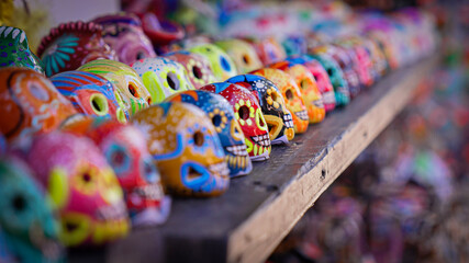 Row of colorful dia de los muertos sugar skulls on wooden shelf at local festival market