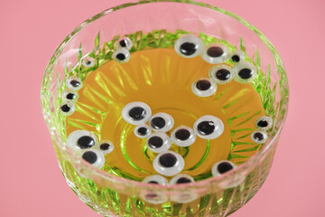 artificial eyes in a glass with a green drink on a pink background. Halloween party decorations