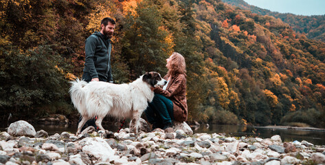 couple with dog enjoying autumn nature by the lake