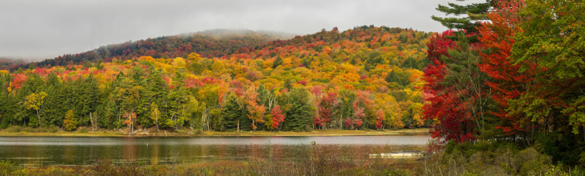 Panoramic photo of hills covered with vibrant fall foliage and water in foreground 