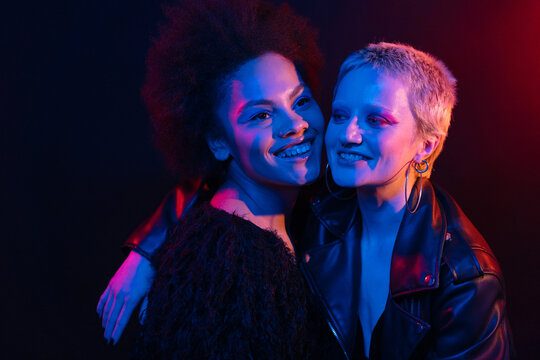 Multiracial girlfriends embracing under neon light