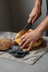 an adult European male baker holds a round fresh bread in his hands. a man in a bakery holds a yeast-free bread on sourdough and a baguette. cool and healthy bread for the whole family. vegan food for