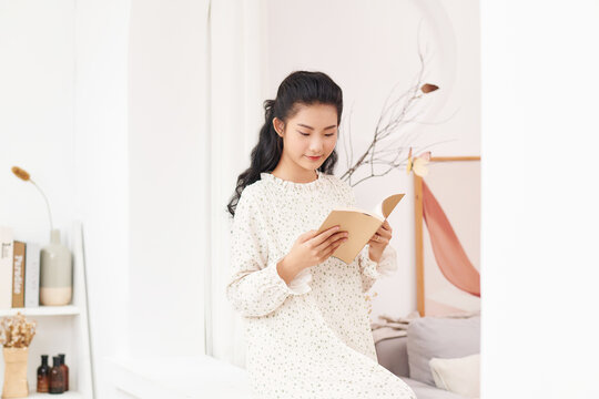 White cozy bed and a beautiful girl, reading a book, concepts of home and comfort.