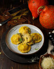 Pumpkin ravioli with ricotta and parmesan. Low key, on a dark wooden background, vertical, with a small orange pumpkin in the background