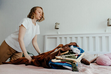 Woman throwing stack of clothes on bed