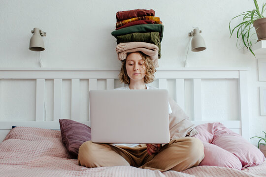 Woman with stack of clothes using laptop