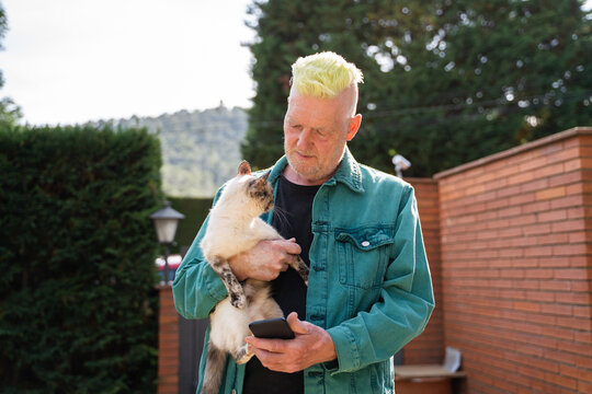 Happy Senior man holding cat and phone  in garden 