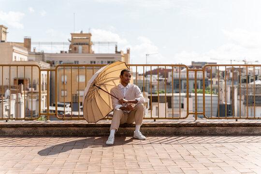 Stylish man sitting posing with an open parasol