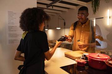 Smiling black customer making contactless payment with smartphone in cafe