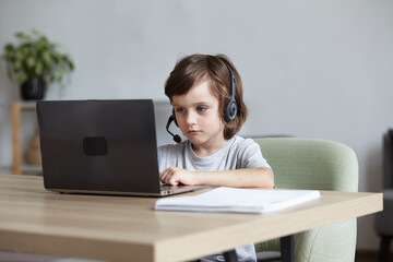 Cute boy learning online remotely by video call using a laptop. A schoolboy pupil kid studying computer work, typing, and programming. A young gamer plays and streams a videogame.