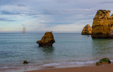 Pinhao Beach in Lagos Portugal in the evening with a sailing ship in the horizon.