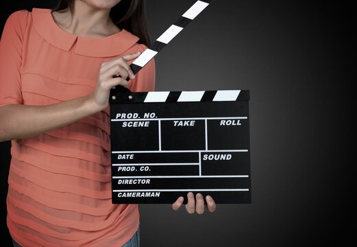 the woman is holding a black clapperboard or movie slate in studio shooting on the background.