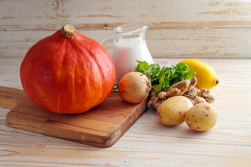Red kuri squash and ingredients for a vegan autumn soup with coconut milk, ginger and coriander for Thanksgiving and Halloween on a wooden table, copy space, selected focus