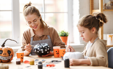 Cute little girl daughter painting Halloween pumpkins with mother at home