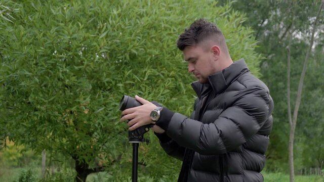 Attractive caucasian photographer in black outfit taking pictures with the green park background