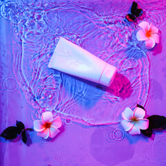 Tube of cosmetic product and flowers in water on color background