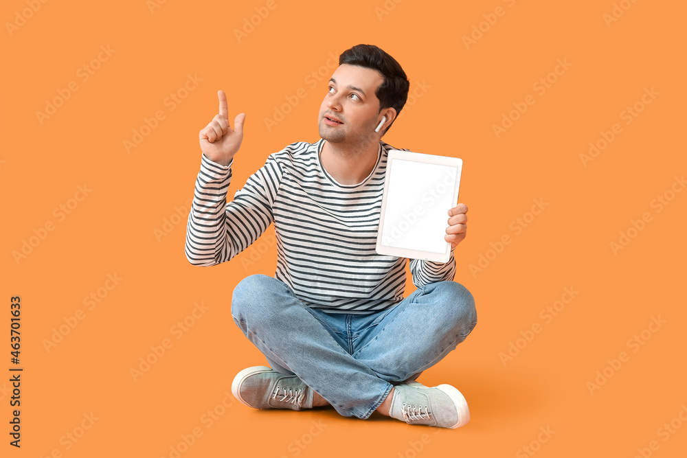 Poster young man with tablet computer and earphones pointing at something on color background