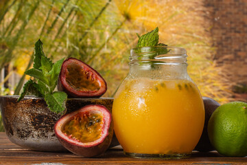 Gulupa or passion fruit juice surrounded by peels and whole and cut fruits, lemons and spearmint on natural background