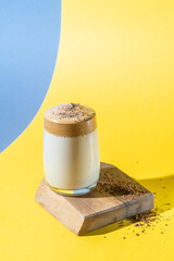 Dalgona coffee with lush foam in a glass on a yellow and blue background. Trendy Korean Drink
