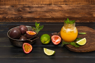 Gulupa or passion fruit juice surrounded by peels and whole and cut fruits, lemons and spearmint on an aged wooden background