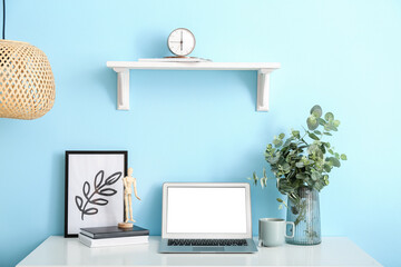 Laptop and vase with eucalyptus plant on table near color wall in room